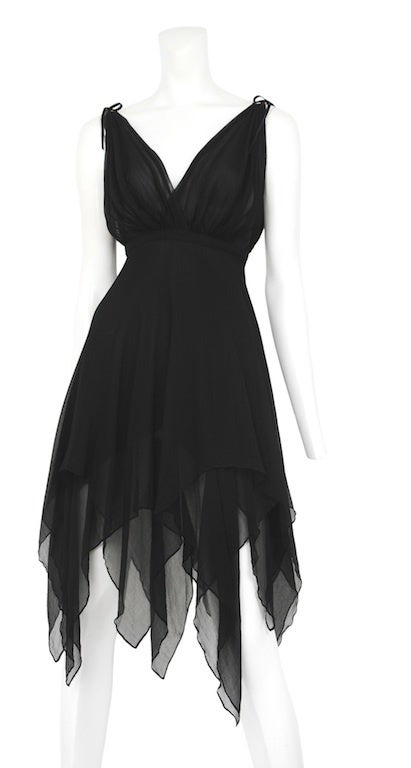 Black chiffon dress with empire waist and handkerchief hem. Straps tie at shoulder with gold circle hardware detail.