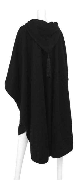 Black heavy wool cape. Large hood with tassel detail and large toggle closure at neck.