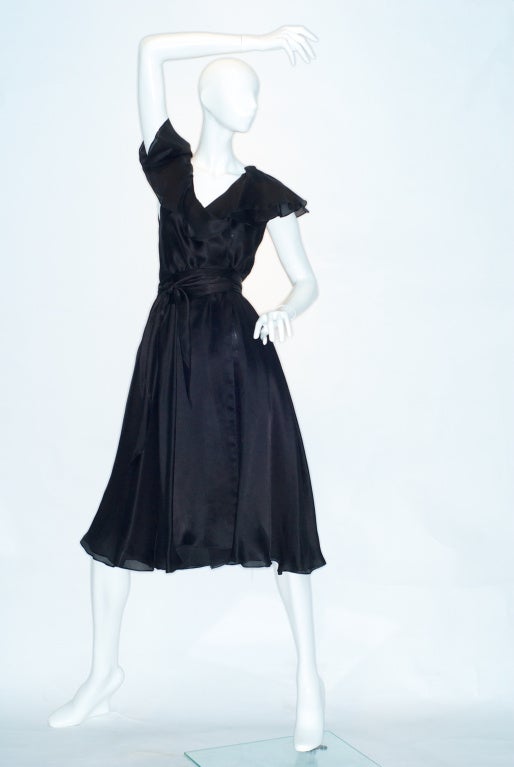 Exceptional black silk satin-faced organza wrap dress.  Circa 1980.  Made with a single seam.  Ruffles frames the neckline.  Sold with matching bias cut scarf belt.
 
Halston became enamored of ruffles in the late 1970s and early 1980s. WWD
