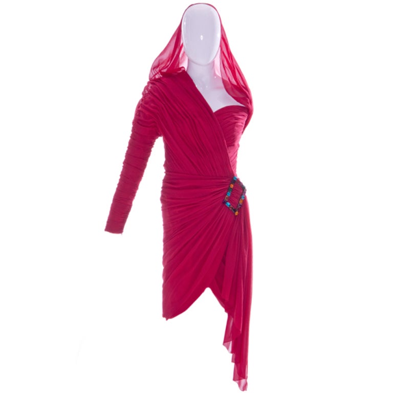 A CHRISTIAN LACROIX FOR JEAN PATOU RASPBERRY SILK CREPE COCKTAIL DRESS, WITH HOOD, FALL/WINTER 1985-86
labelled 'Jean Patou Paris' with swathed wrap-over bodice, single long sleeve, asymmetric neckline, largejewelled buckle to one hip,
condition ;