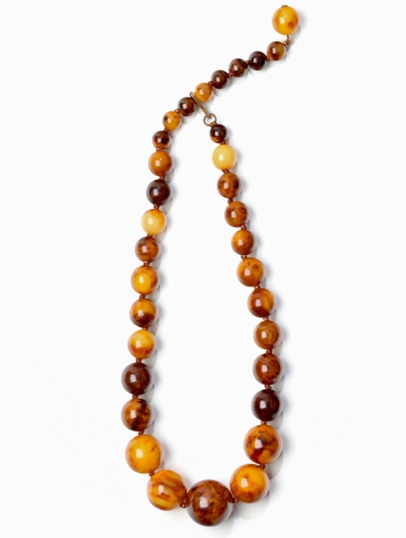 A juicy strand or Marbleized Butterscotch Bakelite Beads strung as a choker sold with a later matching pair of Marbleized Butterscotch Bakelite half hoop earrings which are circa 1960's.