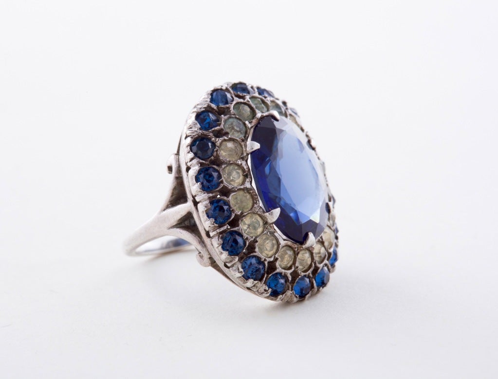 A Stunning Art Deco Cocktail Ring by Ciner, the massive faceted center stone flanked by a dazzling array of smaller blue and white pastes all set within a sterling silver mount, the quintessential Jazz Age Bauble, signed Ciner. 

Ring Size 6.5