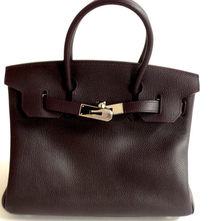 This Hermes Raisin Clemence Leather Birkin Bag is 30 cm size with palladium hardware. The front clasp is stamped HERMES-PARIS, and on the reverse side of the clasp is the blind stamp 