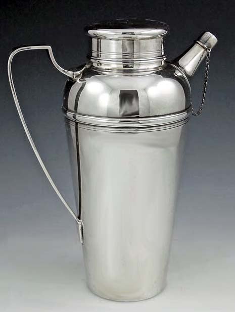 Tiffany Art Deco Sterling Silver Cocktail Shaker, C.1920, Tiffany & Co, New York. The plain tapering body with ribbed upper section and cover, half shield handle, the spout with silver stopper and chain attached. Height: 9 ½ inches. Weight: 25 ¼ oz.