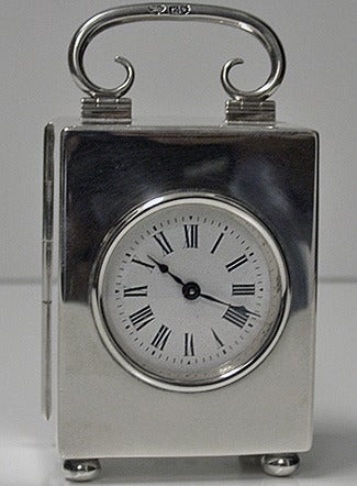 Silver Carriage Clock, London 1913, by The Goldsmiths and Silversmiths Co. Ltd. The plain rectangular Clock on four bun feet with hinged plain scroll design handle, solid hinged back cover with circular white enamel dial and black roman numerals.