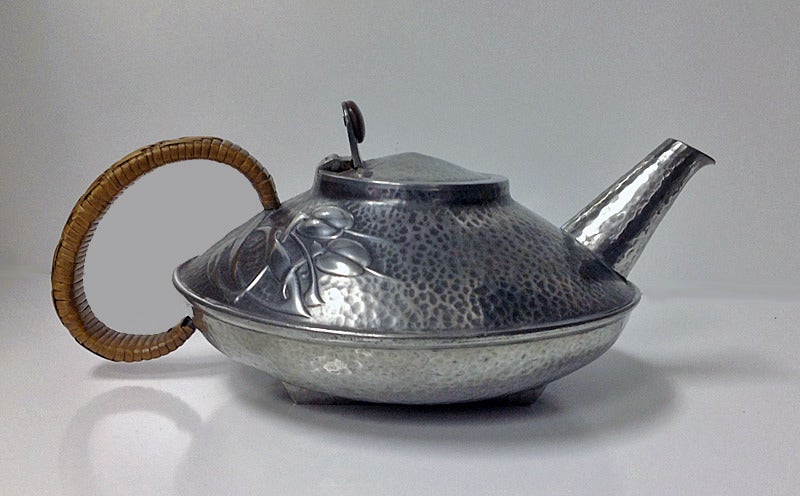 Archibald Knox Liberty Tudric hammered pewter tea set, C.1906.Teapot, cream jug and sugar, each of compressed oval form with relief whiplash curved celtic ornament interlace decoration, original wicker handle and button to teapot. Stamped 6 Made in