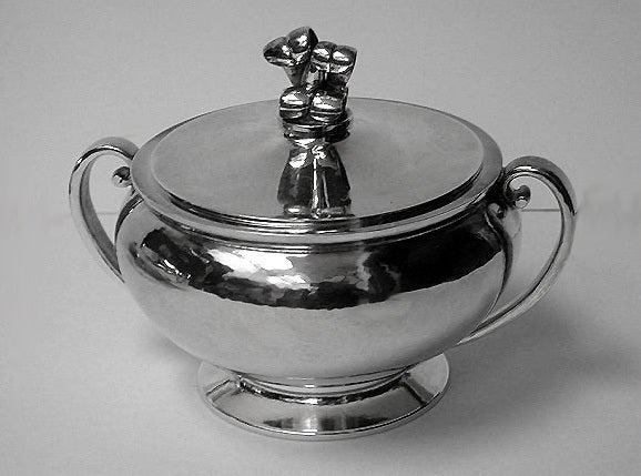 Danish Silver Coffee Service C.1930 by Evald Nielson, comprising Coffee pot, covered two handled sugar bowl and cream jug. Each piece, hammered silver, circular spreading footed base with plain scroll handle, plain baluster body, bud foliate motif