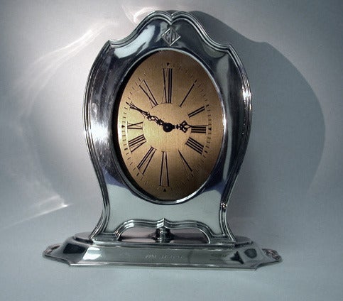American Art Deco Sterling Silver Desk Timepiece, Reed & Barton, circa 1920s. The large timepiece on elongated reeded base supporting a silver shield-shape frame, gilt dial, Roman numerals. The sterling mount with monogram ED in art deco style and