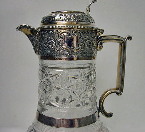 Antique English Silver parcel gilt and Glass Claret Jug, hallmarked, Sheffield in 1896, Walter & Charles Sissons. The Claret Jug mount and hinged cover chased with trailing scroll foliate motifs centering on either side of the collar a vacant scroll