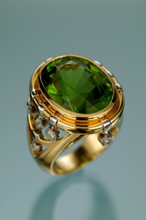 A remarkable 20.65ct Peridot, showcased in a playful hand crafted ring, accented by 0.43ct of dangling diamonds in 