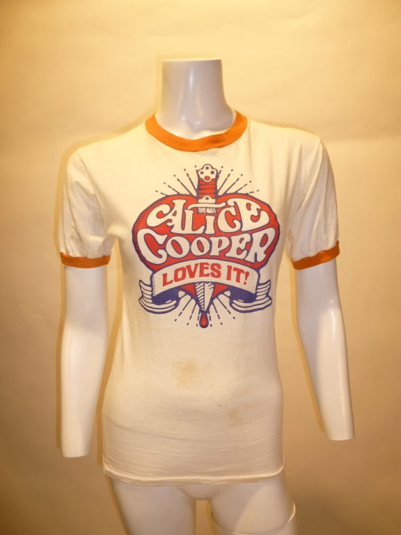 Vintage 1972 Alice Cooper Loves It! T-shirt for their fifth studio LP School's Out. There is some fairly significant staining on the front of the shirt on the stomach area.