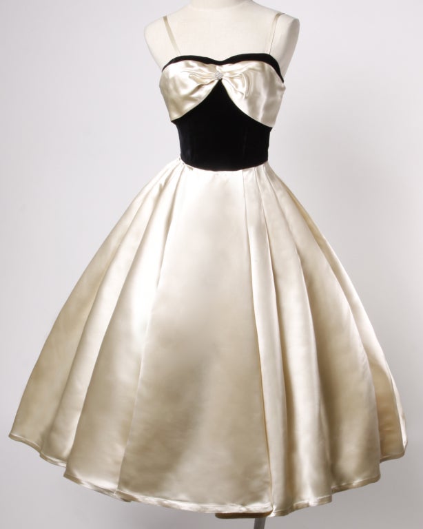 Description: Dance the night away with this dreamy swing dress from days gone by. A symphony of creamy ivory silk satin and luscious black velvet come together in this beautiful 1940s dress. Accented with a rhinestone detail at the décollage. Boned