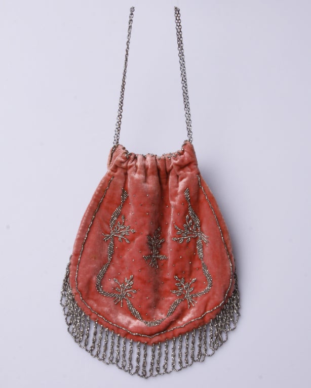 A ladies evening bag of coral silk velvet with a drawstring chain and steel cut beaded accents. This was the height of fashion in 1910! The interior of the bag is finished in ivory satin silk that is still in tact but suffers from a tiny bit of