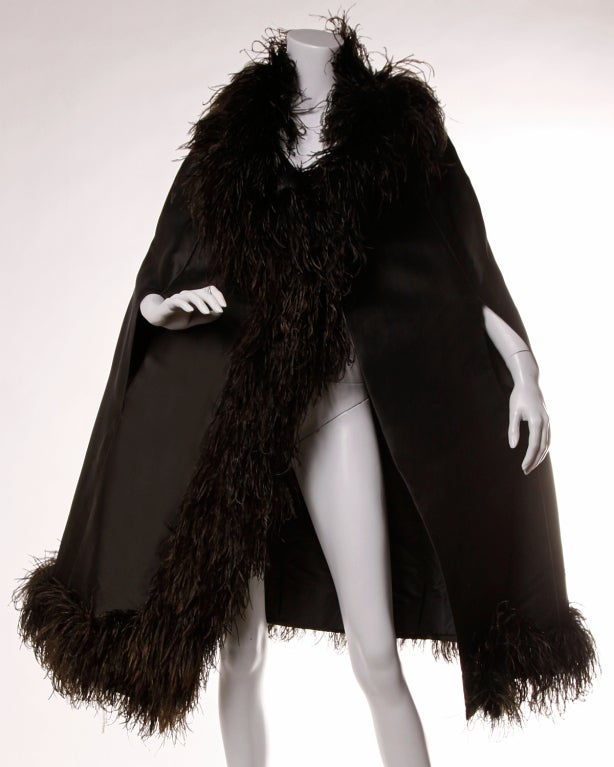 Museum-quality 1960's black silk cape coat with ostrich feather trim by Elizabeth Arden. Fully lined in silk and with hand stitching throughout. Single button closure at the front of the neck. 

Arden's in-house designer in the early 1960's was