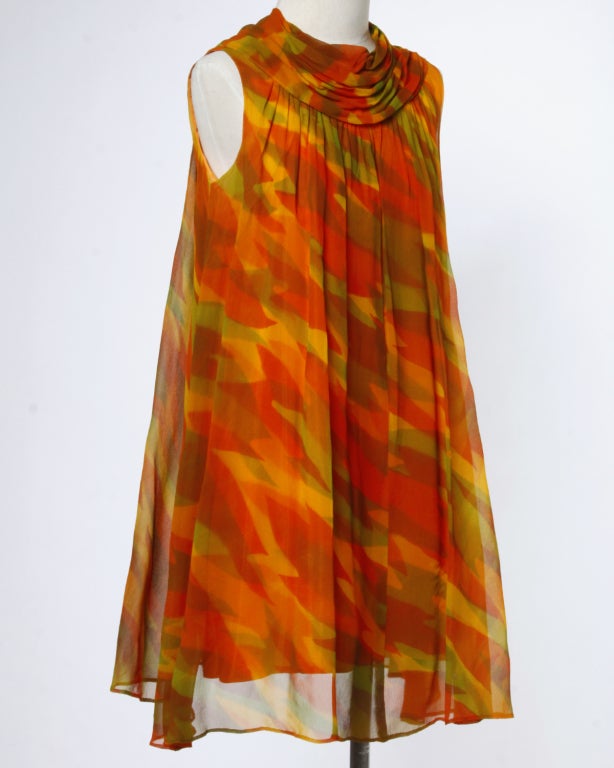 Stunning! Gorgeous silk chiffon trapeze dress from the 1960's in shades of orange, yellow and green. Features a draped collar matching fabric covered buttons down the back and a very 1960's trapeze silhouette. Fully lined with back button