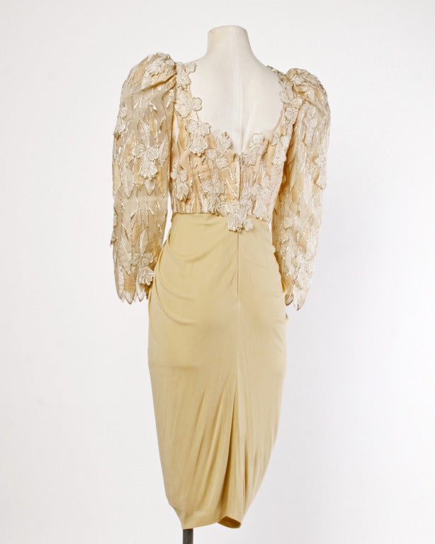 Pretty nude jersey silk dress by Ruben Panis with a cocoon ruched skirt, bold shoulders, and metallic embroidered organza leaf and flower appliques. The dress zips up the back and features a scoop neck and long sleeves. Fully lined.