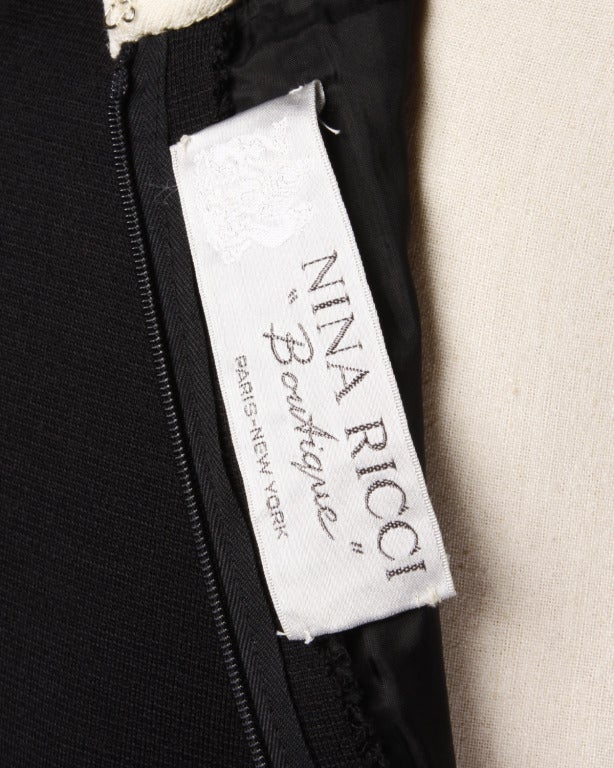 In light weight black and off-white wool, this 1960s vintage Nina Ricci shift dress features a diamond shaped collar and graphic patchwork embellishment near the waistline. It is fully lined in luxurious black silk and zips and hooks up the back