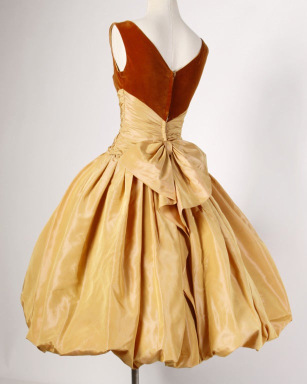 Stunning butterscotch iridescent silk taffeta formal dress from the 1950s with a velvet shelf bust, ruched bodice and extraordinary bubble hem. The dress is fully lined and features a built in crinoline for extra poof! Rear metal zip closure with