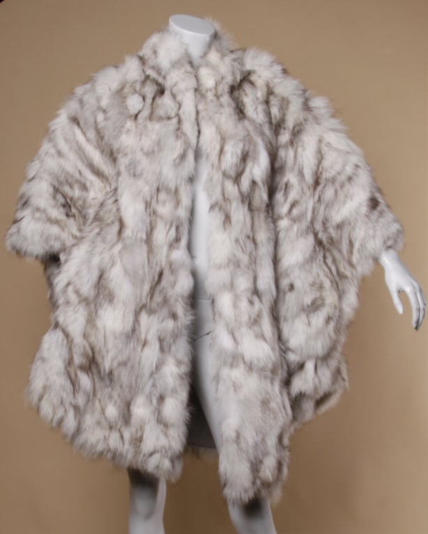 Oversize sectional fox fur coat by Saga Fox. Fur pieces are gray and white and are sewn into pieced leather. Batwing poncho sleeves and chic avant garde shape. Fully lined with a gray nylon lining. Front hook closure. This should fit all sizes on