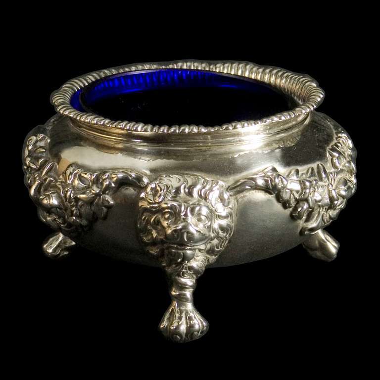 A pair of large heavy Victorian silver salt cellars with applied floral swags and lion mask legs with paw feet,the interiors gilded and with blue glass liners.
