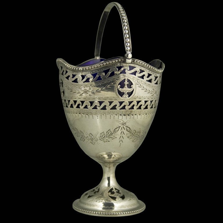 A Victorian Sugar Basket with blue glass liner,of helmet form on pedestal round foot, hand pierced and decorated with hand engraved bright-cut decoration.