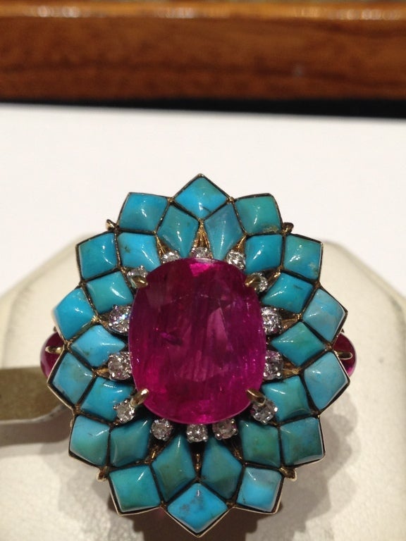 An exquisite cocktail ring centering a natural oval cut ruby (6.55 cts), sided by smaller brilliant cut diamonds, embellished by a turquoise turtle shell shaped structure. 18k gold mounting. Circa 1960.