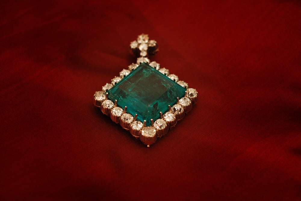 An extraordinary antique pendant of prestigious provenance (refer to certificate in pictures), manufactured in the first half of the 19th century, presenting a unique Colombian emerald weighing 87.50 cts, sided by old mine cut diamonds weighing a