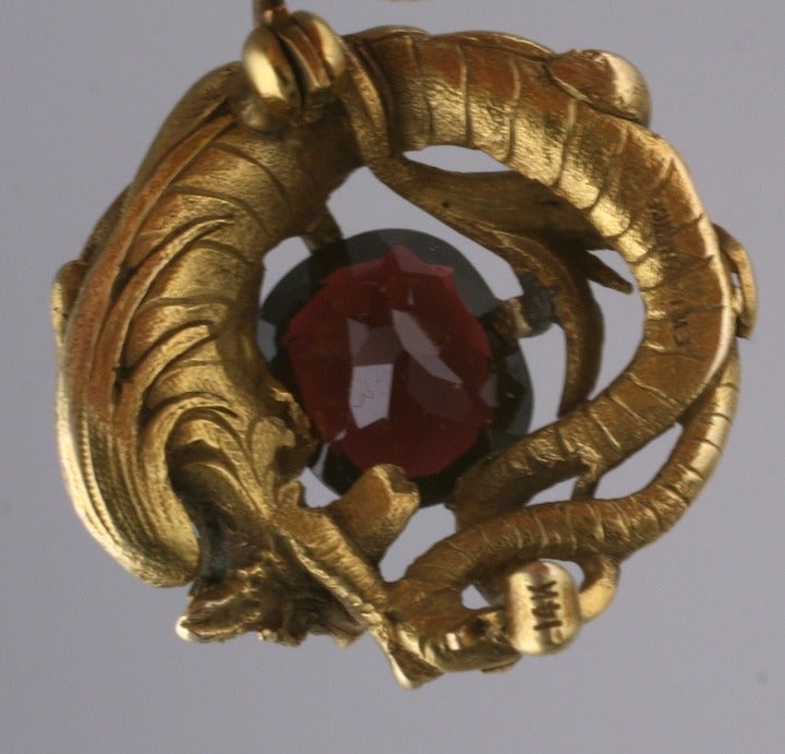 This brooch is by Master jeweler and designer, Gustav Manz who is recognized for his exquisitely detailed representations of the animal kingdom. 
This Art Nouveau chimera clutches and fiercely guards a large cushion cut garnet. The depth and