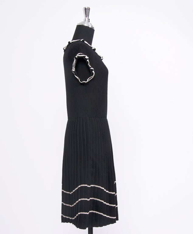 Wool Chanel dress with a pleated skirt and silk ribbon details to collar and sleeves. Also includes a small sparkling Chanel logo to the side and 3 horizontal stripes on the bottom of the skirt.