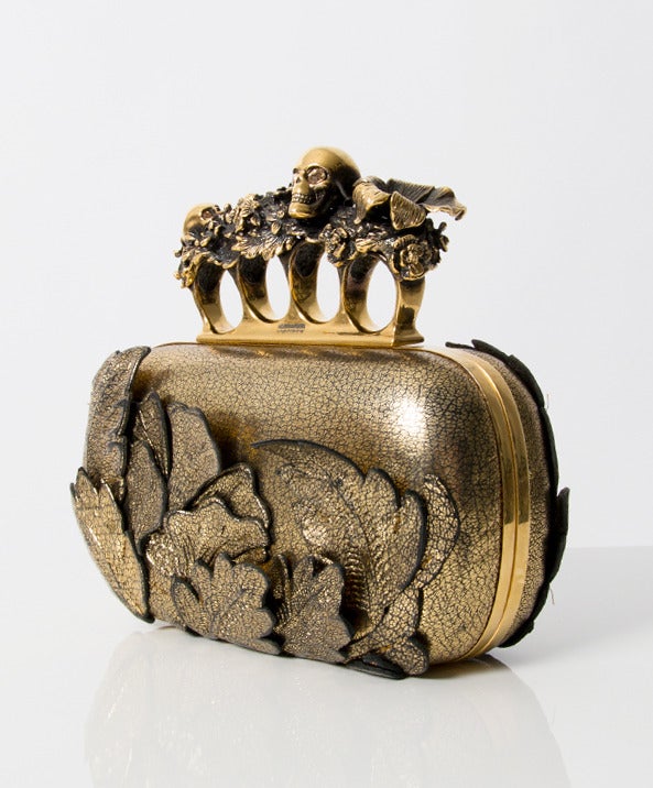 A luxurious handbag which seems very special and comfortable. It combines fragile elements as the golden leather flower and leafs cutouts with brutal,hard elements such as the skull on the clutch.