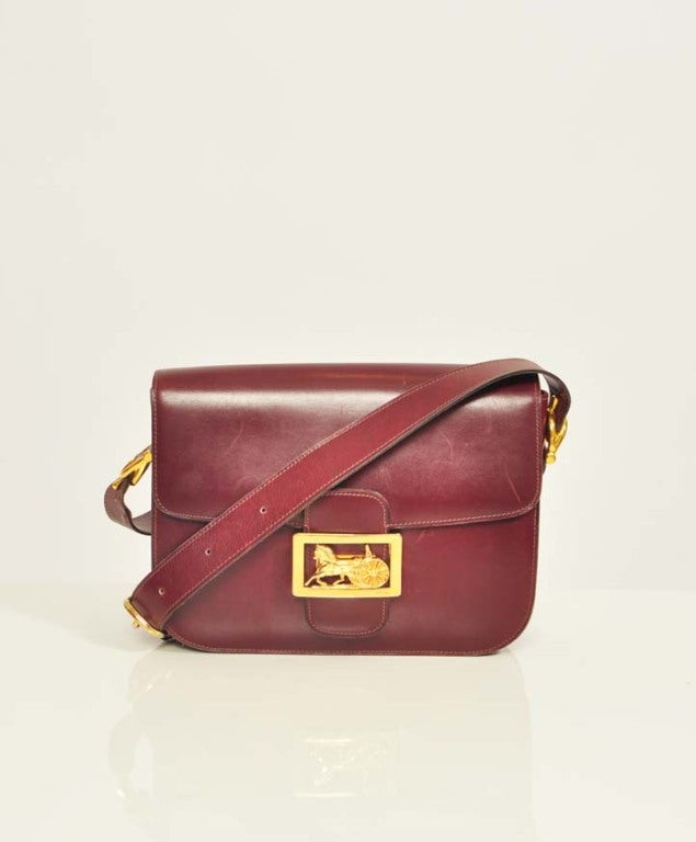 This Burgundy Leather Celine Handbag is a beautifully crafted classic Celine bag, featuring a unique square horse and chariot clasp. The bag is spacious and features three compartments with three pockets. It also features a small compact mirror