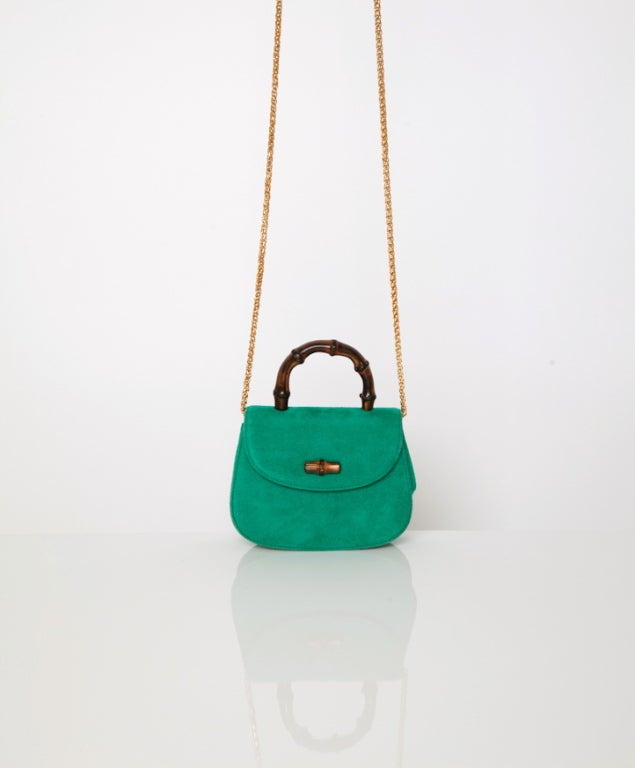 Small Gucci evening bag in green suede. Handle is made of wood and on the flap there is also a wooden detail. The flap can be closed with a press button. 
The gold tone shoulder strap, hidden on the inside, makes it easy to wear. 
Perfect handbag