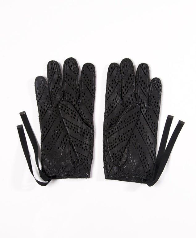 A pair of black gloves featuring lasercut leather and ribbons to tighten around wrist.