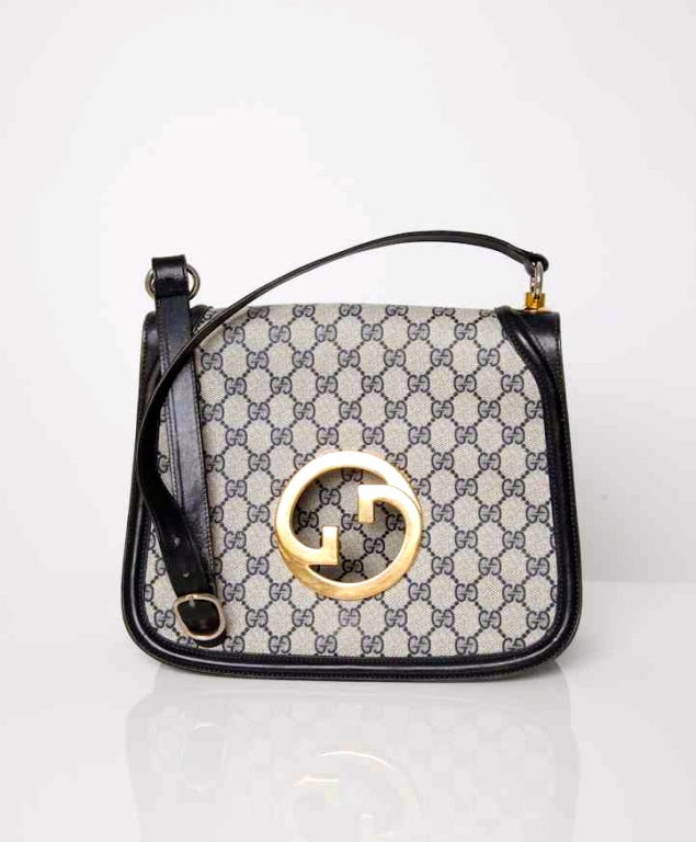 This shoulder bag with navy blue monogram is unmistakably Gucci and is a classic piece. The adjustable shoulder strap is secured to the handbag with gold tone hardware. The famous Gucci insignia on the flap is also gold tone. The flap can be closed