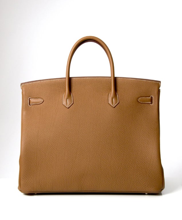Este precioso bolso Hermes Birkin de piel de Togo en tono dorado luce herrajes de paladio. El famoso bolso está en perfecto estado, se ha comprado hace muy poco y nunca se ha usado. Se entrega con chubasquero, documentos de autenticidad, clochet y