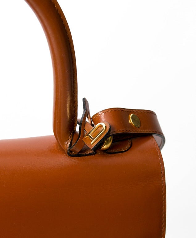 Delvaux Brillant MM Handbag with attachable shoulder strap. Yellow gold hardware. The color is best described as a deep cognac or light fox red hue. 

On the occasion of the 1958 Brussels World Fair, Delvaux created a stir with the launch of a new