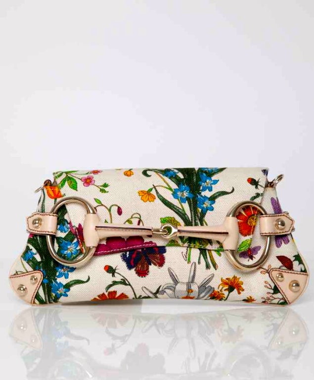 A colorful clutch with flower print by Gucci. The clutch has beige leather details with gold tone studs and rings on the outside and beige leather lining inside. Carry this beautiful clutch in your hand or under you arm and give your outfit an
