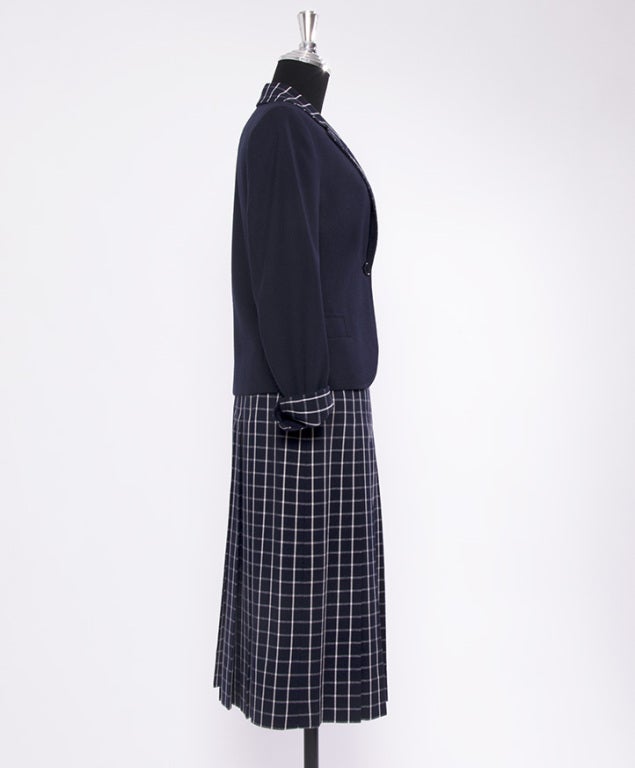 2-piece skirt suit in navy blue and white.
Short vest with checkered collar.
Knee-length pleated skirt in check pattern with leather and gold hardware integrated belt.