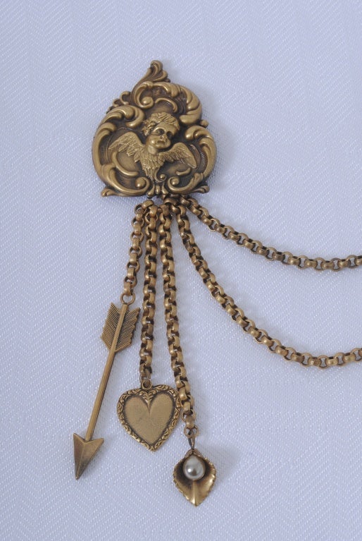 Joseff of Hollywood double brooch, each depicting a repousse cupid among scrolls, connected by a double chain. Suspended from one of the brooches on chains is an arrow, a heart, and a petal with pearl center.

Cupid medallions: width: 1 1/2,