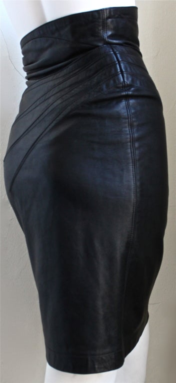 Jet black leather skirt with brass buckle designed by Azzedine Alaia dating to 1986. Fits a US size 2. Approximate measurements are as follows: waist 24