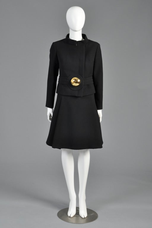 Spectacular circa 1969/70 Pierre Cardin black wool suit. Boxy cropped jacket with asymmetric closure, nehru collar + space age top stitched, attached circular belt. High waisted, a-line skirt. The best part, of course, is the massive gold brooch at