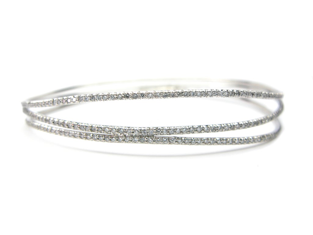 Three elegant rows of diamonds gracefully flow away and towards each other, occasionally touching to create a solid bracelet. The piece has 2.38 carats of round diamonds all set in 18K white gold. This beautiful 3 row diamond bangle will be sure to
