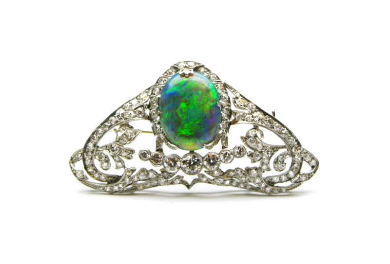 This one-of-a-kind platinum Art Deco from the early 20th-century pin features an exquisite 18mm x 14mm black opal center surrounded by prong and bezel set Old European Cut diamonds. The pin's delicate filigree design will add a touch of elegance to