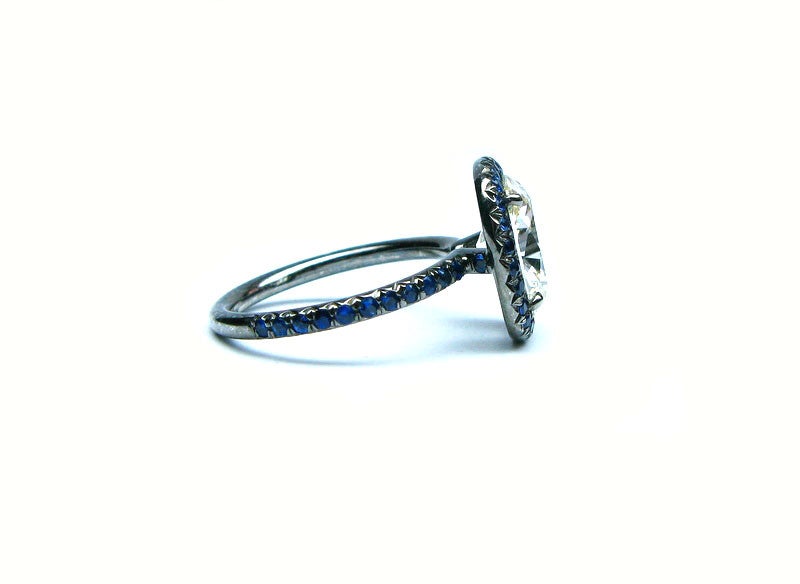 This unique 3.02ct M color VS1 clarity cushion cut diamond is set in an oxidized platinum ring and is framed by 1.35ctw of blue sapphires.This ring is a new twist on the classic frame ring and would make the perfect statement piece for a fashion