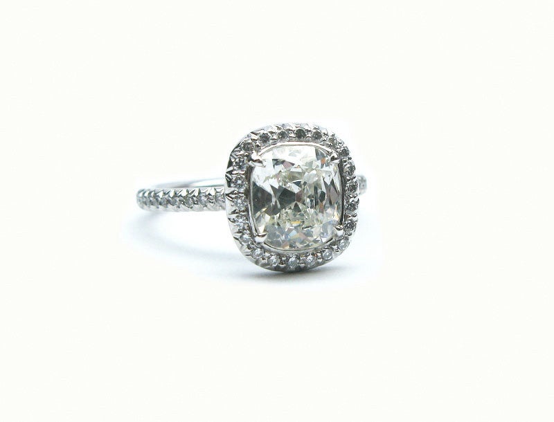 This lovely 1.80 carat K color SI1 clarity cushion cut diamond is framed by 0.53 carats of pave diamonds, and is set in a platinum and diamond ring. This classic and feminine ring looks great on any woman.