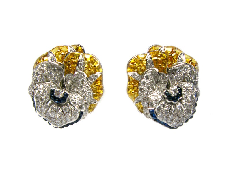 These exquisite pansy floral design earrings feature round brilliant diamonds,  blue sapphire cabochons and yellow sapphire trapezoids set in platinum. These elegant earrings are the perfect statement piece for a sophisticated woman on the town.