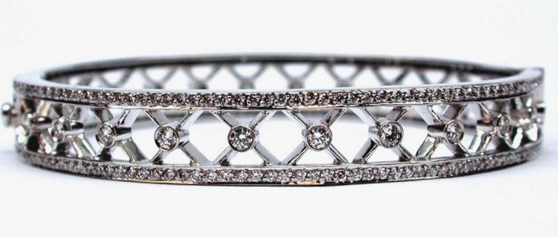 This unique 18kt white gold bangle features pave and bezel set diamonds weighing 3.30ctw in a decorative criss-cross pattern. Add this beautiful piece to your collection today!
