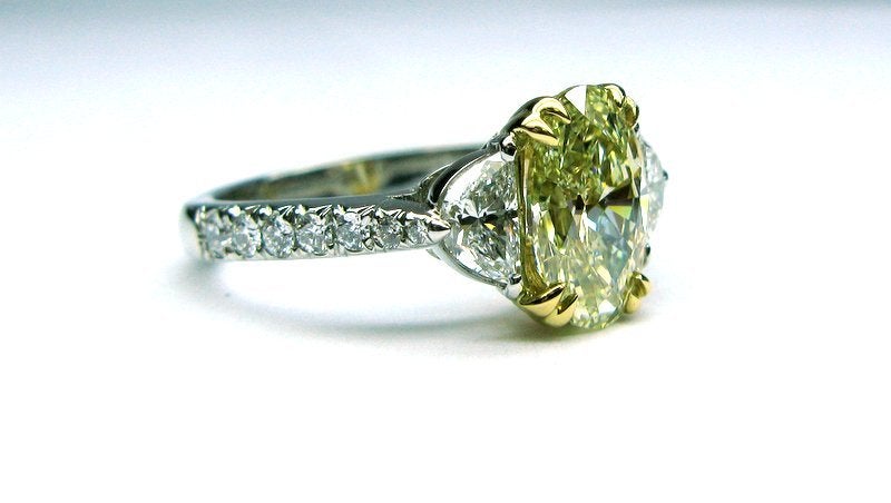 This classic 1.52ct VVS2 clarity fancy yellow oval diamond is flanked by two white diamond half moons on each side totaling 0.49cts set in 18k. The platinum band contains 7 graduated round diamonds on each side totaling 0.24cts.