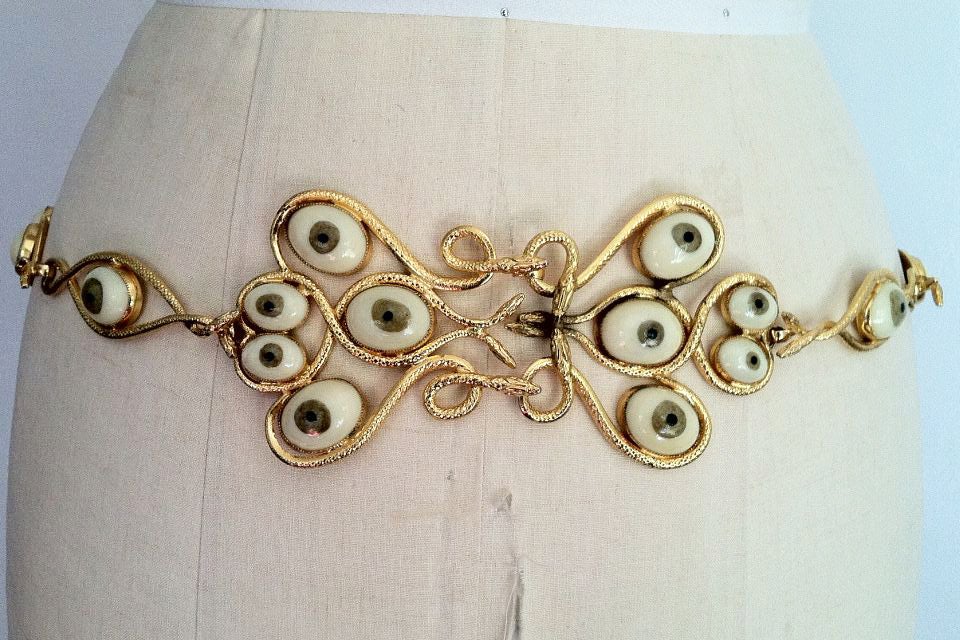 A rare prototype vintage William de Lillo surrealist 'eye' link belt. Authentic gilt metal 'snakes' linked item mounted with pate de verre glass 'eyeballs'. Hidden front hook closures. Belt size 34