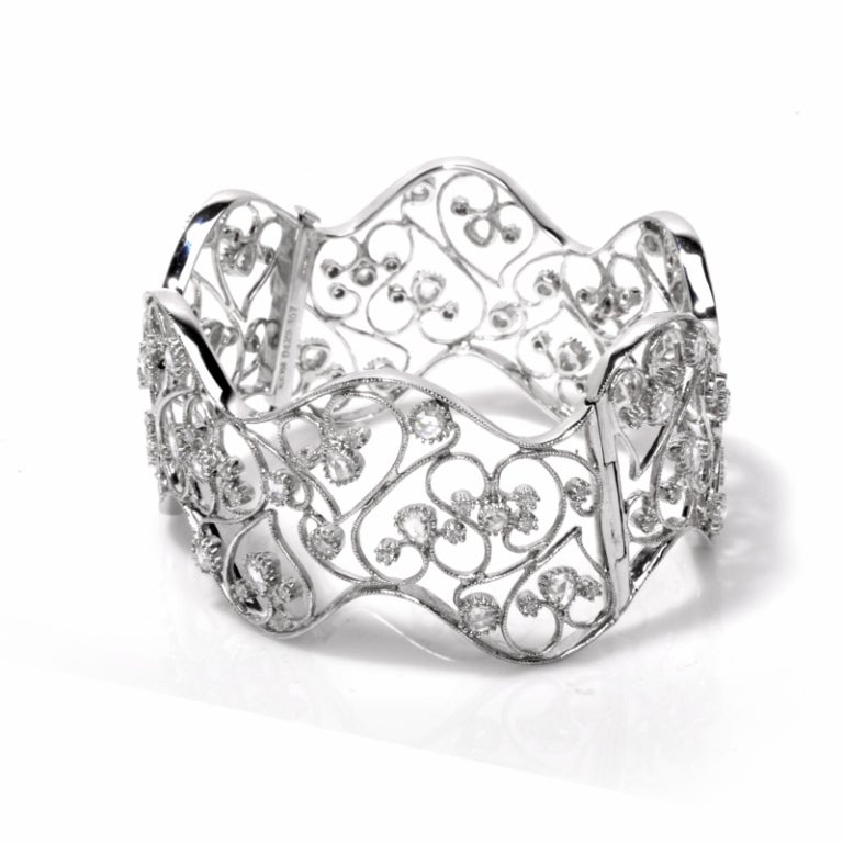 Elegantly designed and sparkling diamonds make this intricate and exquisite bracelet a joy to own. Finely crafted in solid 18K white gold, this wide bracelet features a wave design that is set with milgrain heart scroll work accented with a total of